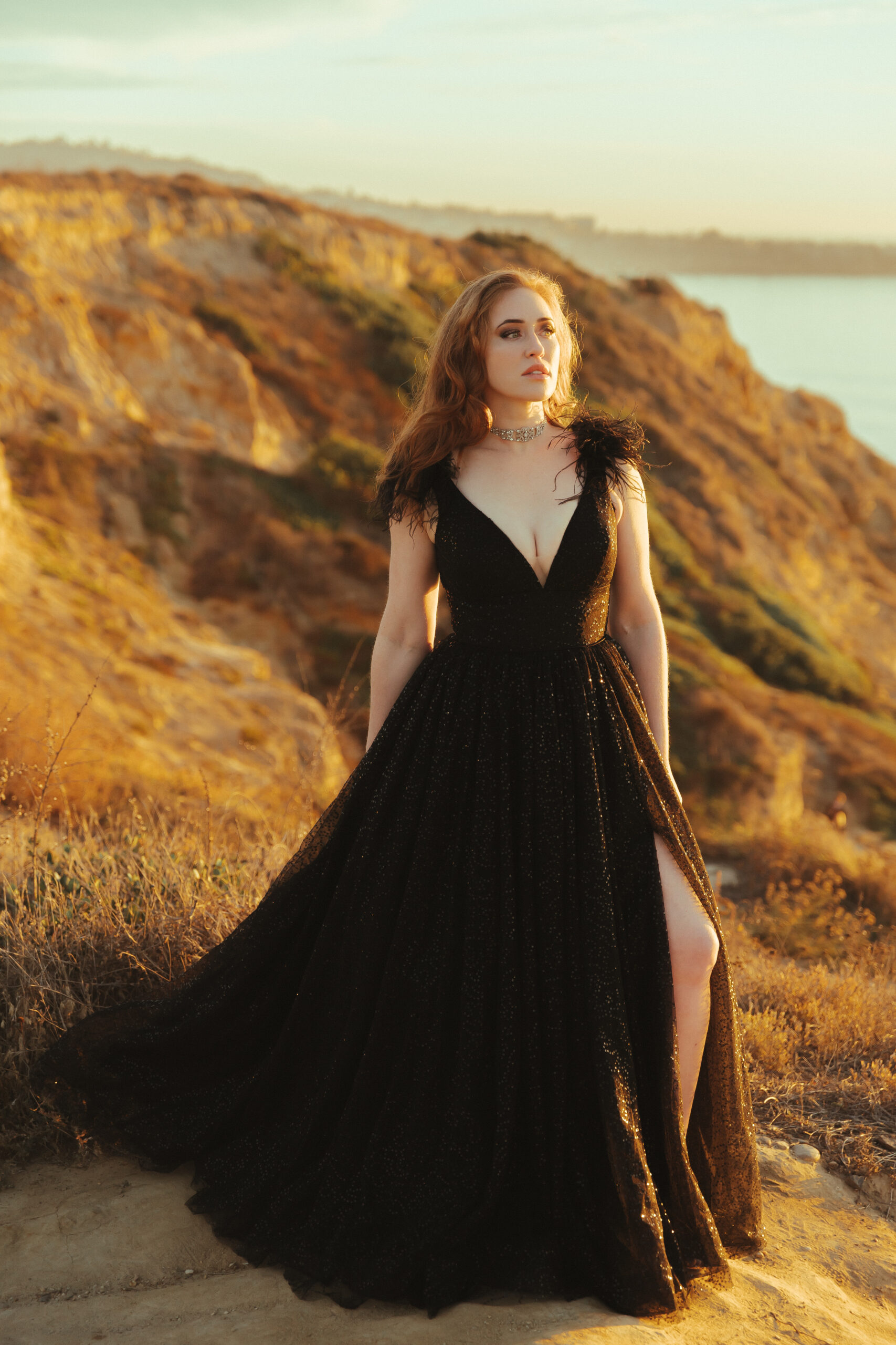 a woman in a long black dress on a cliff next to the ocean